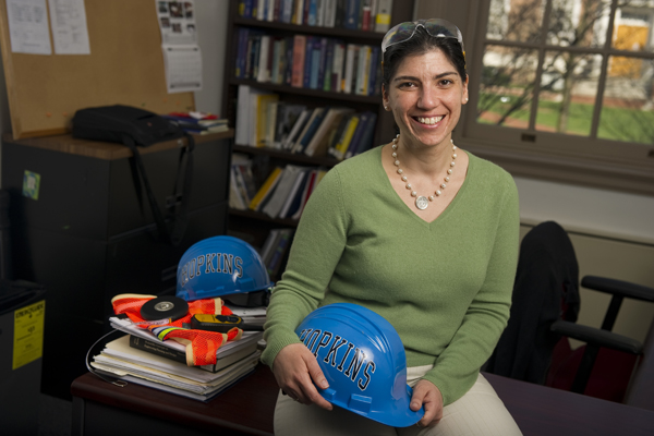 Judith Mitrani-Reiser with pieces of the ‘uniform’ she wore daily in Chile: safety goggles, a fluorescent safety vest and a bright blue Hopkins hard hat. Photo: Will Kirk/Homewoodphoto.jhu.edu
